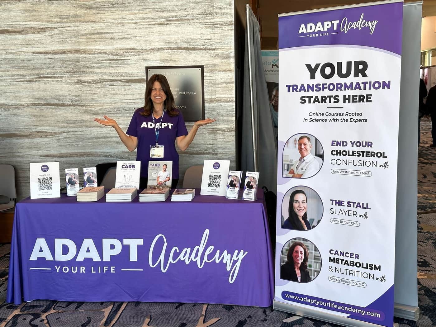 Adapt Academy stand at a show: a purple table cover and a roll-up banner headed Your transformation starts here, with course leaflets on the table