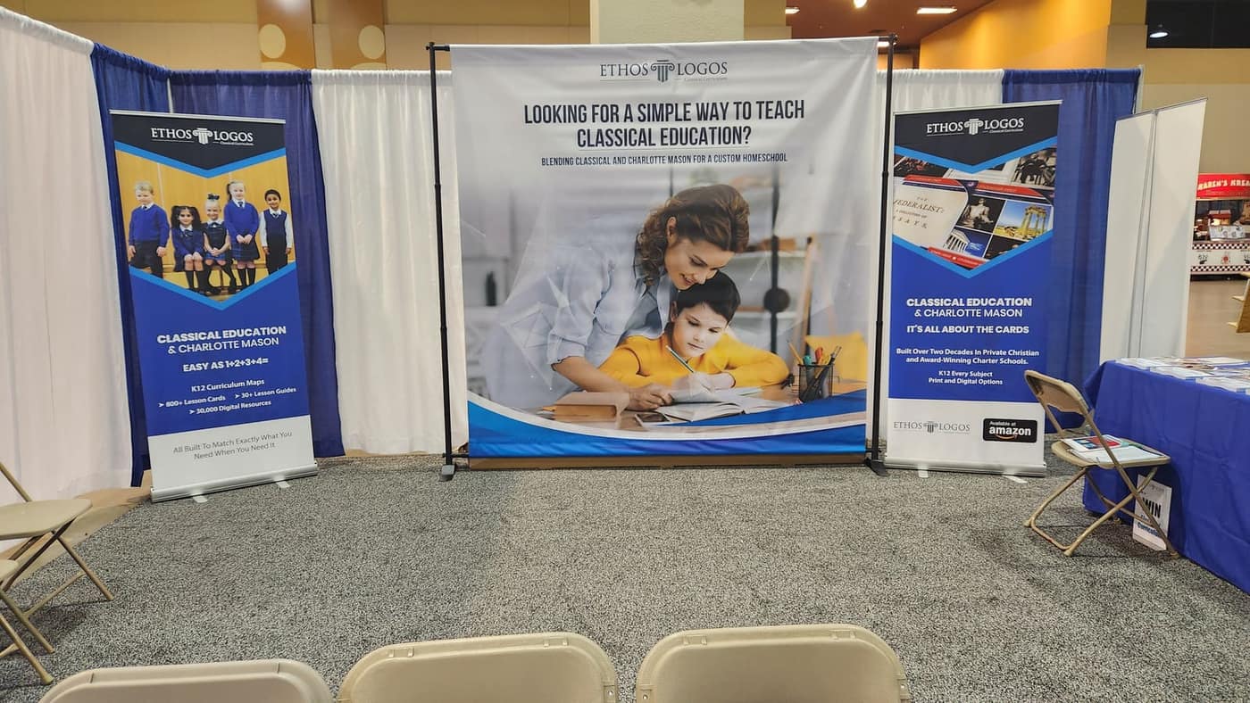 Ethos Logos stand at a show: a backdrop headed Looking for a simple way to teach classical education, between two blue roll-up banners