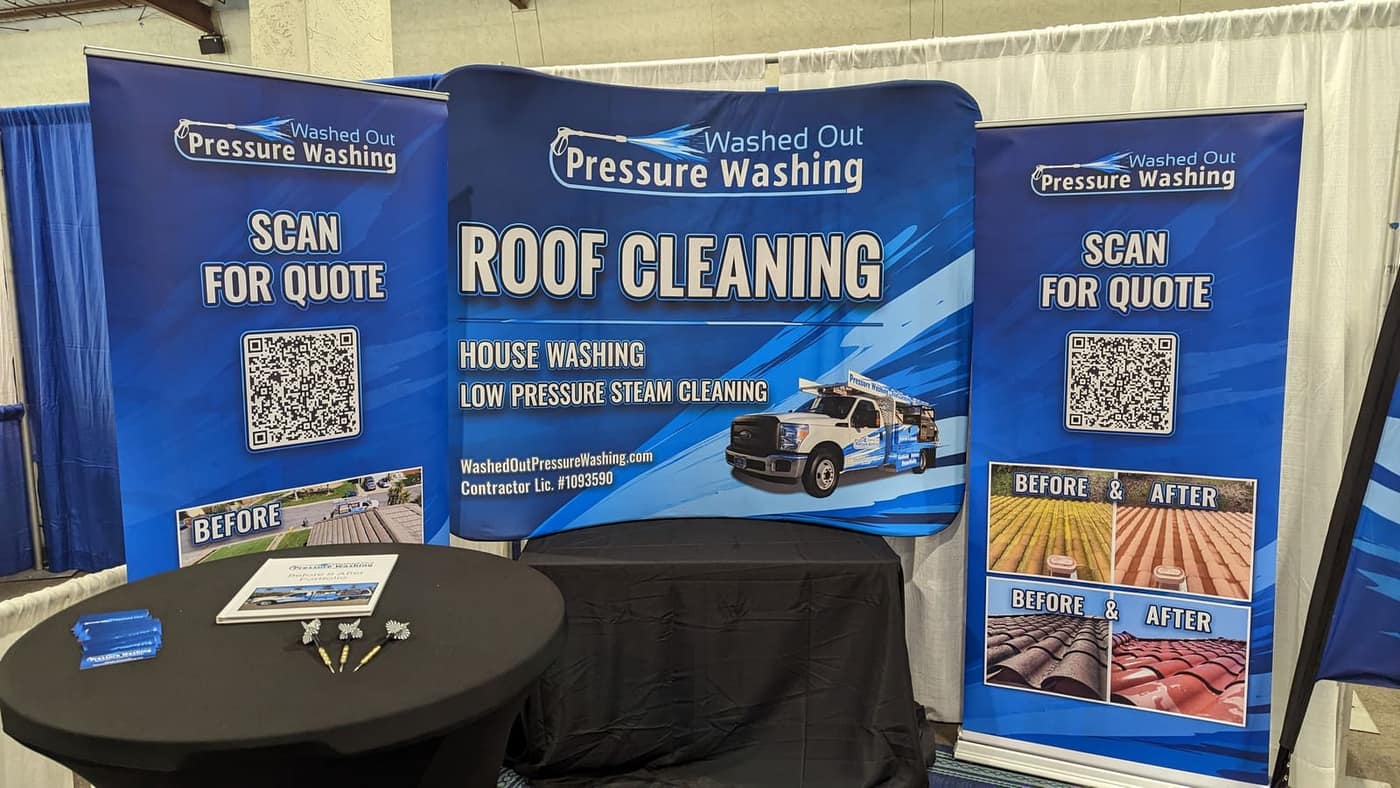 Washed Out Pressure Washing stand at a show: a roof cleaning backdrop between two roll-up banners with Scan for quote QR codes and before and after photos